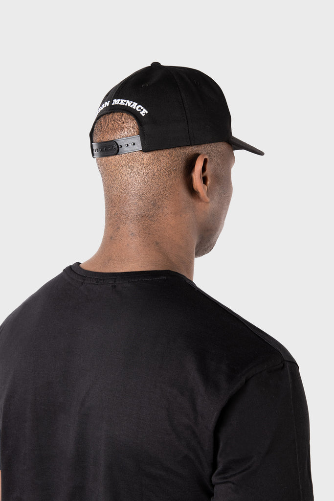 Wearing a black Maison Menace Signature Hat by MAISON MENACE and a matching t-shirt, the person stands with their back to the camera against a plain grey background, adding intrigue to the minimalist scene.