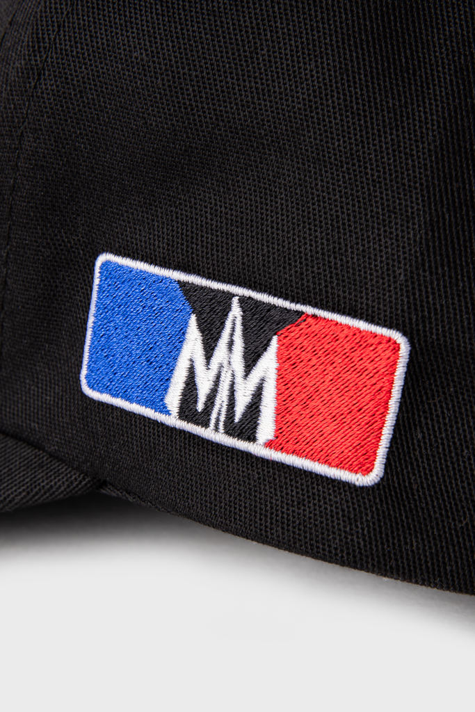 Close-up of the Maison Menace Signature Hat in Black by MAISON MENACE, made from cotton twill. It features an embroidered logo with a blue rectangle on the left, white MM in the center, and a red rectangle on the right.