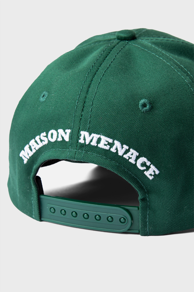 The Maison Menace Signature Hat in Cactus is a green baseball cap with MAISON MENACE embroidered in white on the back and an adjustable snap strap for a perfect fit.