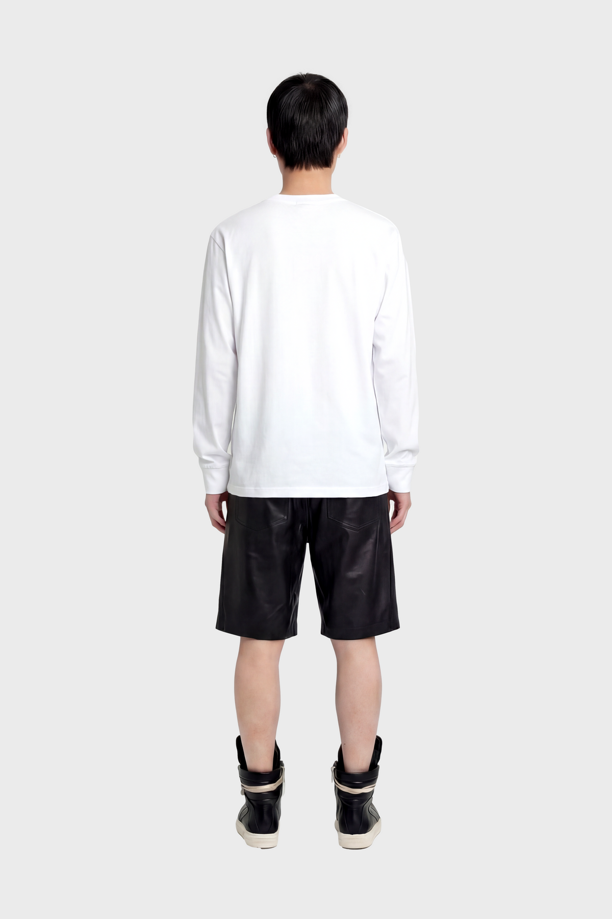 Person wearing a white long-sleeve t-shirt and black leather shorts on a white background