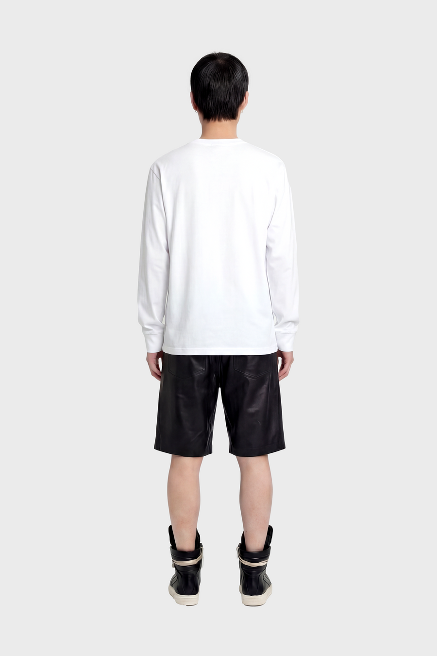 Person wearing a white long-sleeve t-shirt and black leather shorts on a white background