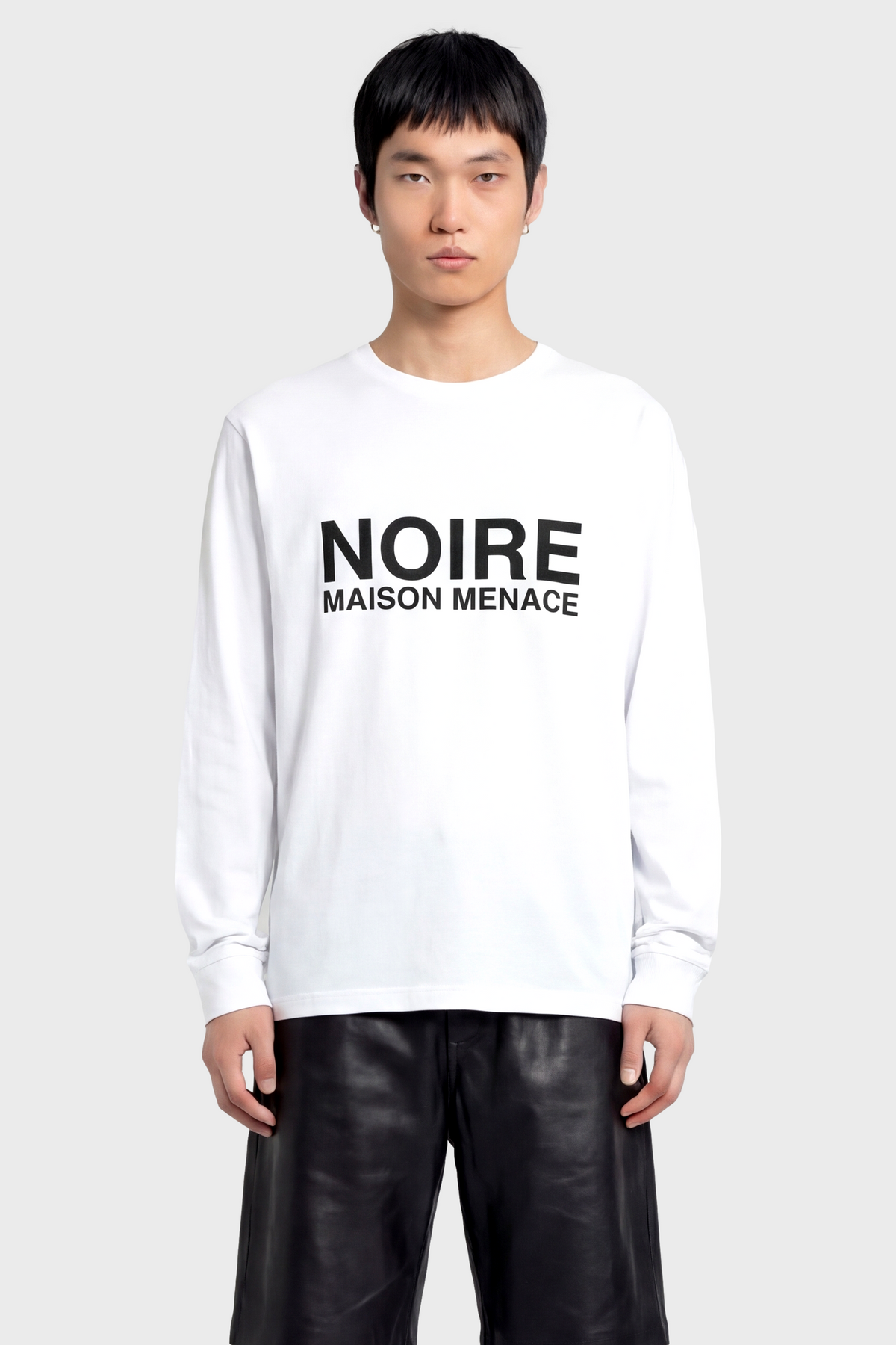 Person wearing a white long sleeve t-shirt with 'NOIRE MAISON MENACE' text on a plain background