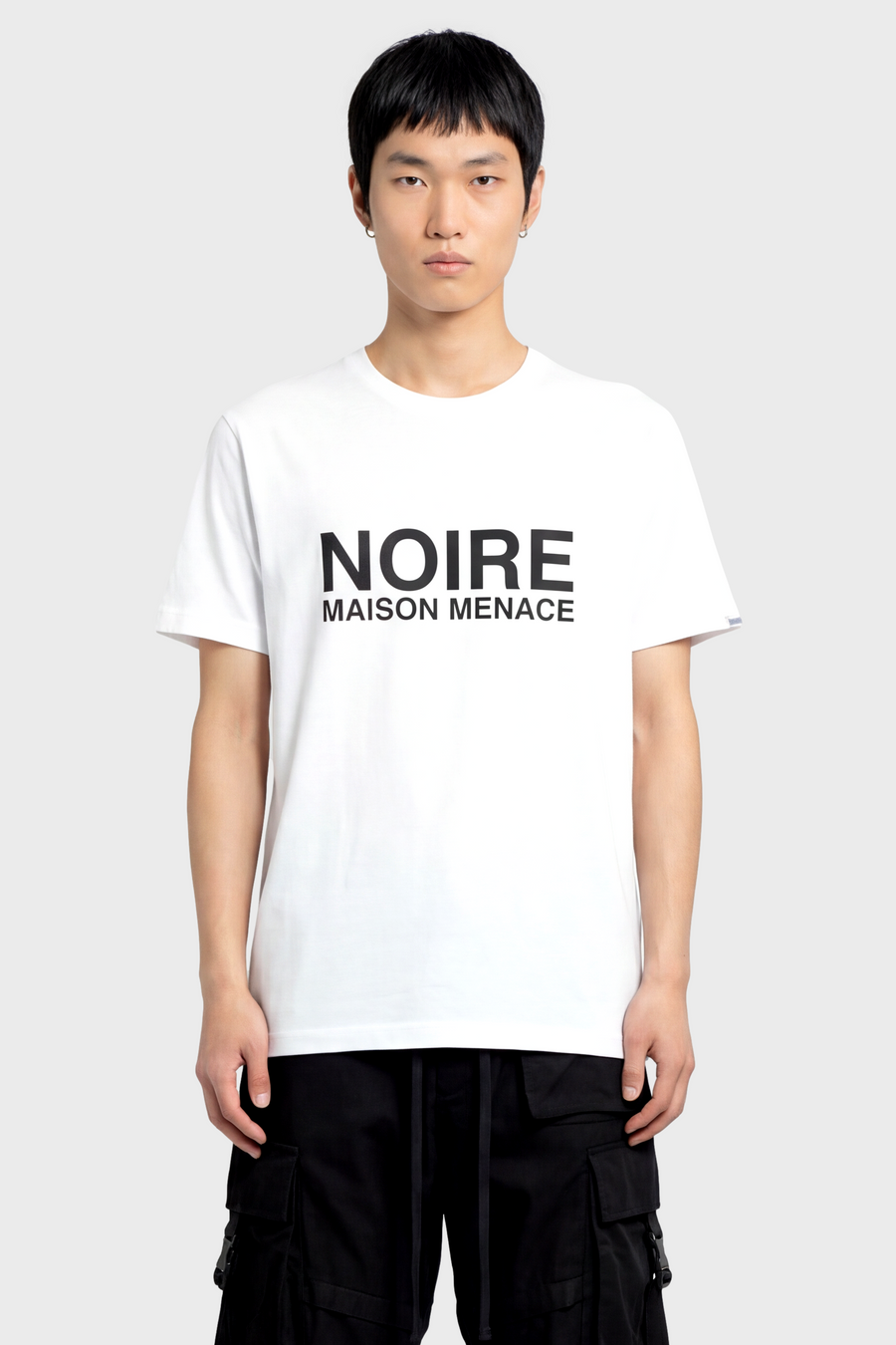 Person wearing a white t-shirt with 'NOIRE MAISON MENACE' text on a plain background