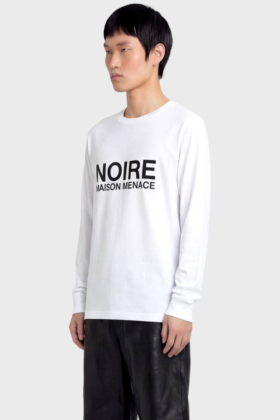 Person wearing a white long sleeve t-shirt with 'NOIRE MAISON MENACE' text on a plain background