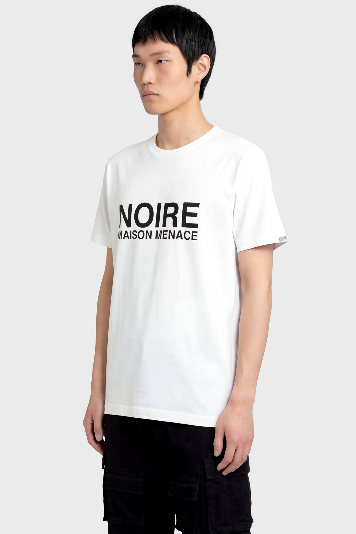 Person wearing a white t-shirt with 'NOIRE' text on a plain background