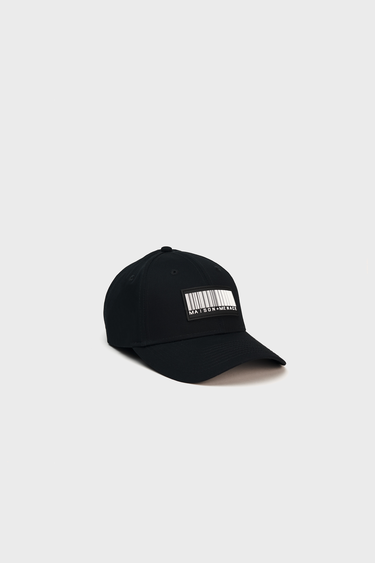 The Maison Menace Classic Hat by MAISON MENACE is a black baseball cap made of cotton canvas, featuring a barcode design patch on the front. It is presented against a gray backdrop and includes an adjustable Velcro closure for comfort.